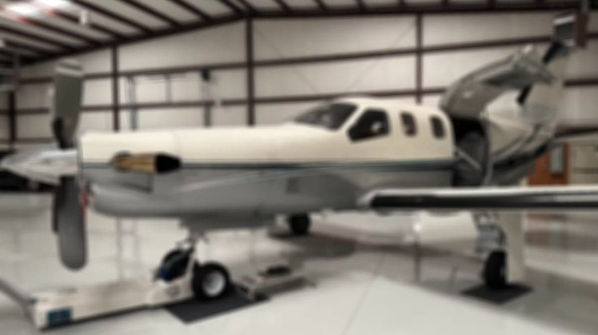 Blurred image of a TBM 850 aircraft in a hangar with the door open.
