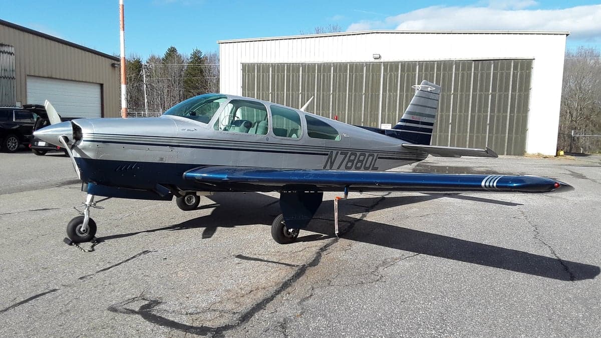 Side view of a silver and blue Beechcraft Bonanza with registration N7880L parked on the tarmac.