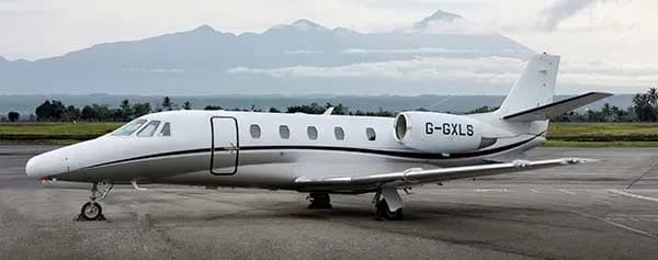 Side view of the G-GXLS Cessna Citation on the tarmac with mountains in the background.