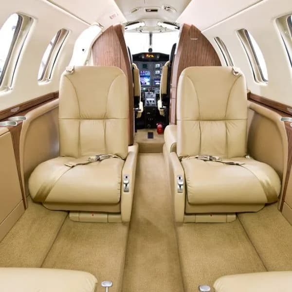 The interior cabin of a private jet with beige leather seats and a partial view of the cockpit in the background.