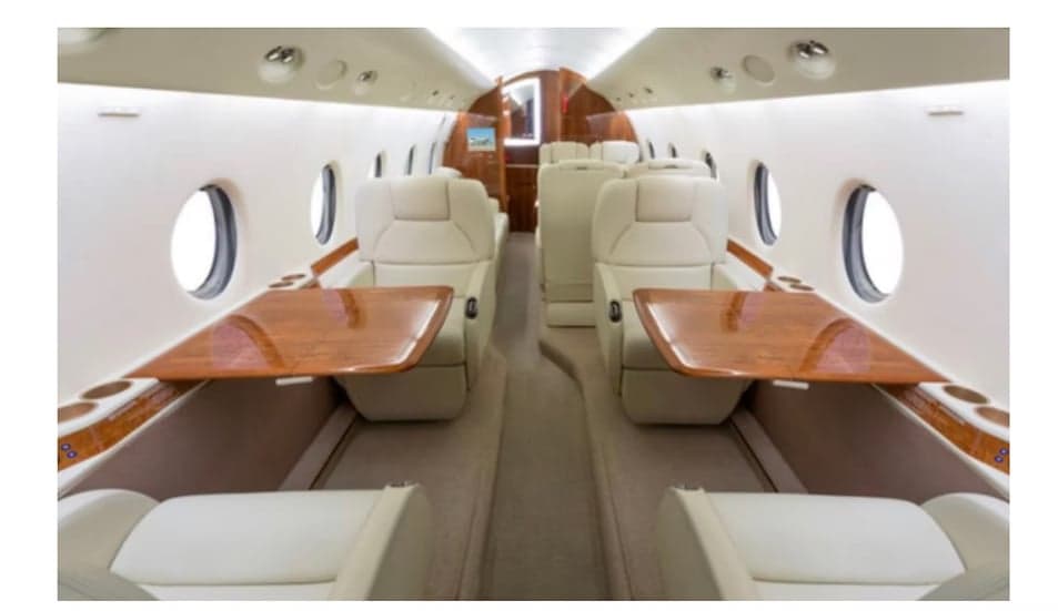 The aircraft's interior features white leather seats and wooden tables.