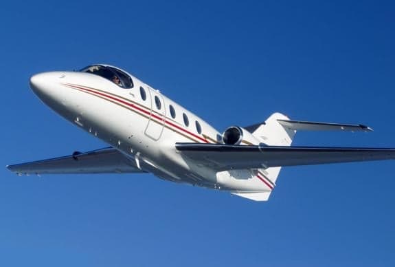 A white jet with red and gold stripes flying in the sky.