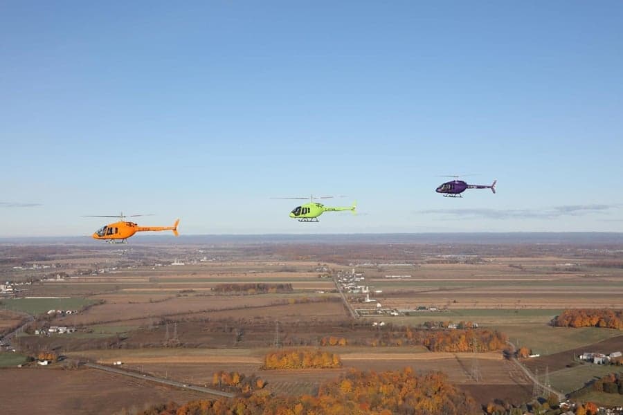 Three helicopters of different colors flying in formation over a rural landscape.