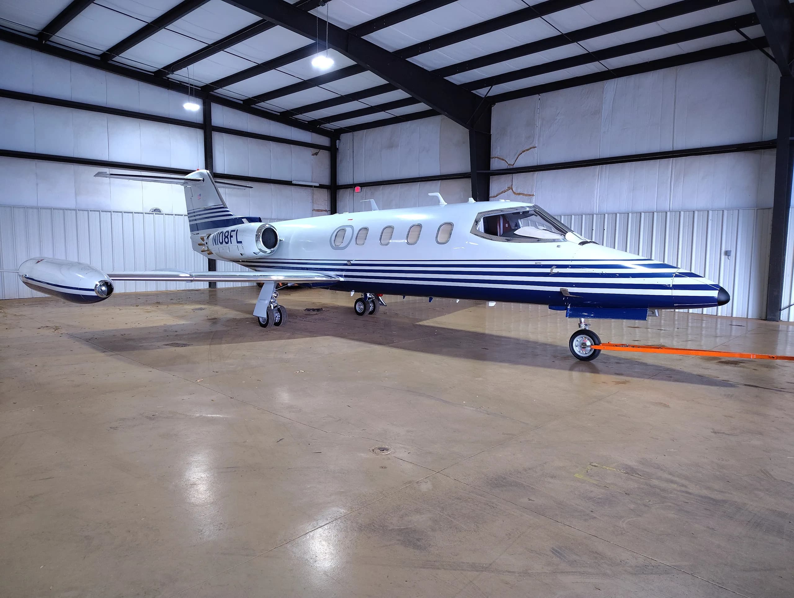 A Learjet aircraft with a white and blue stripe paint scheme parked inside a hangar.