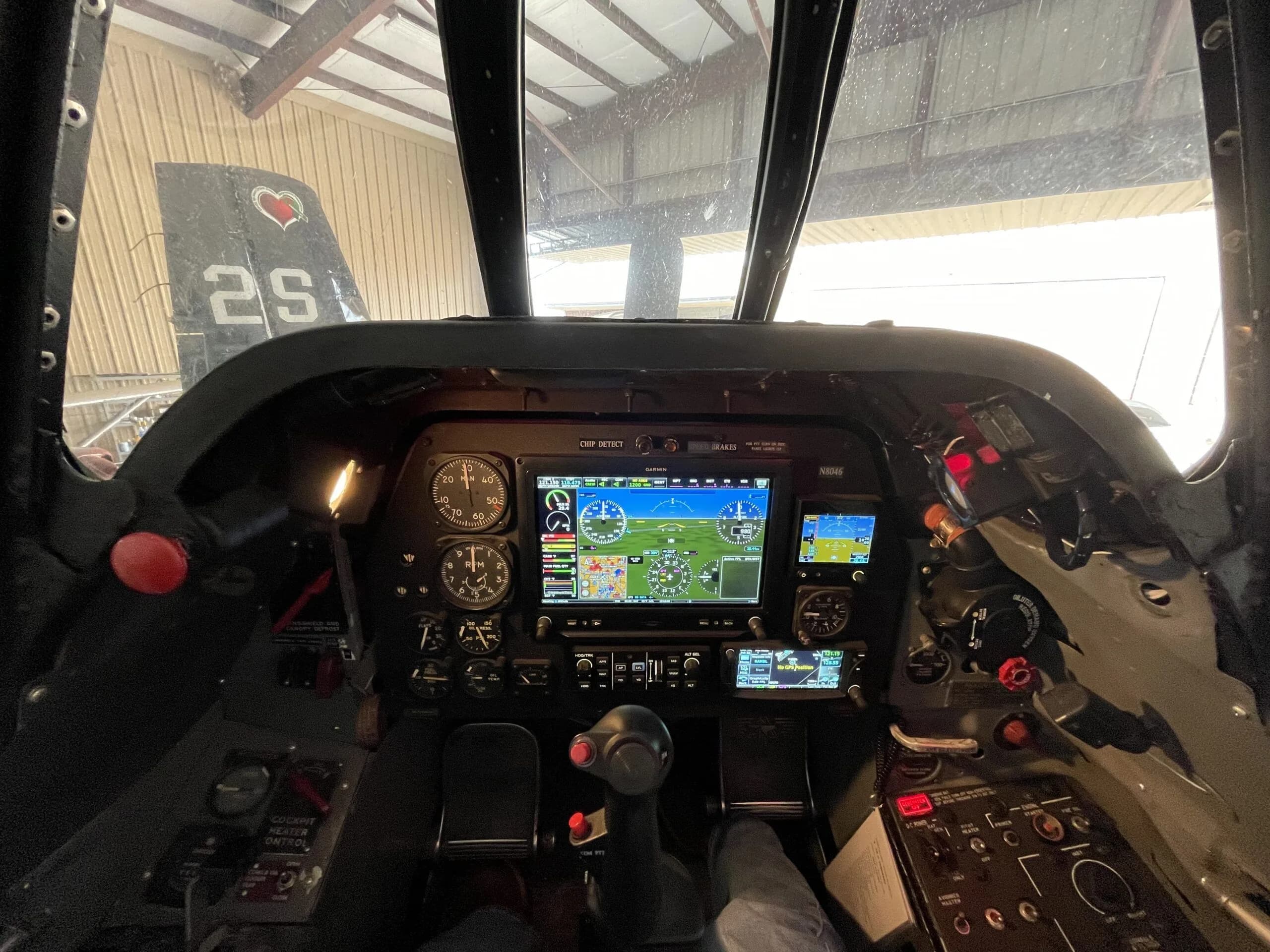 The modern glass cockpit of a T-28 Trojan aircraft, featuring multiple digital displays and traditional gauges, with a view of a hangar outside.