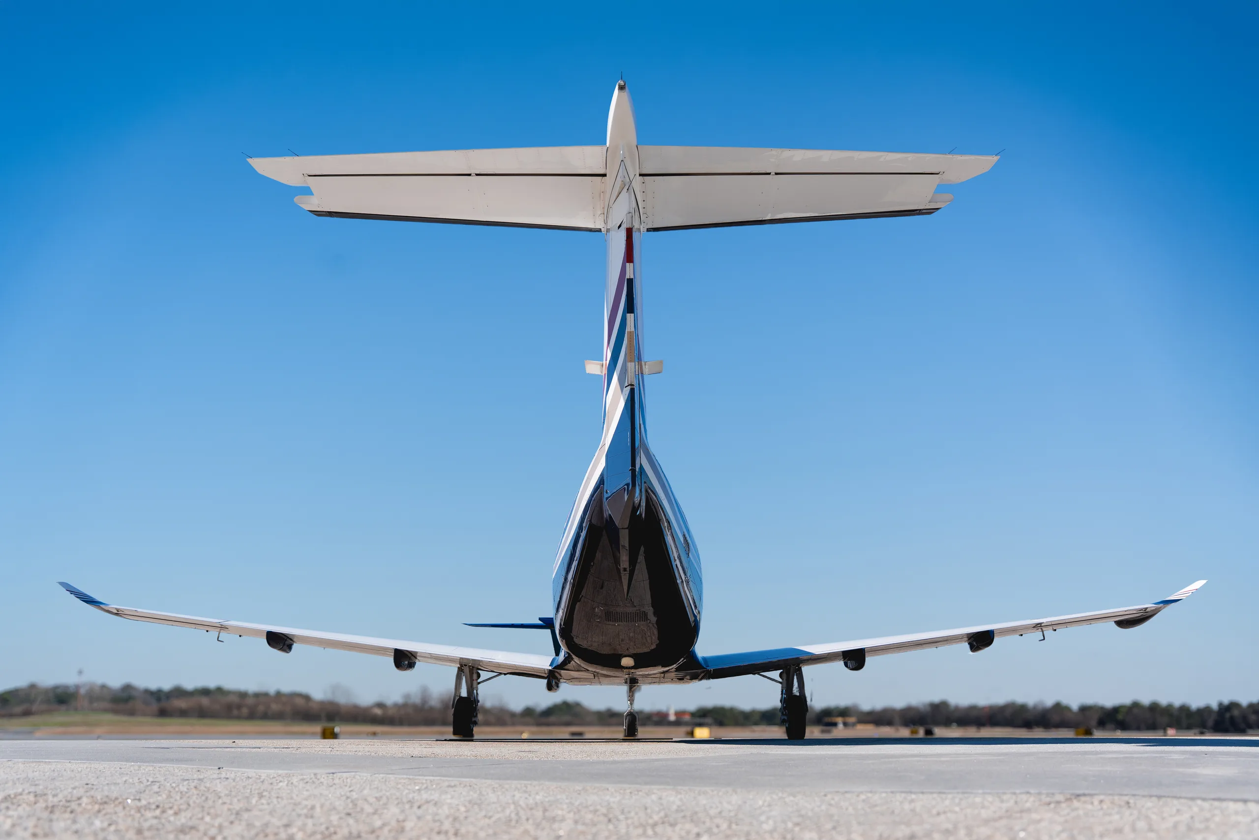 A rear view of the Pilatus PC-12 turboprop aircraft, registration N133PE, showing its tail and wings on an airfield.