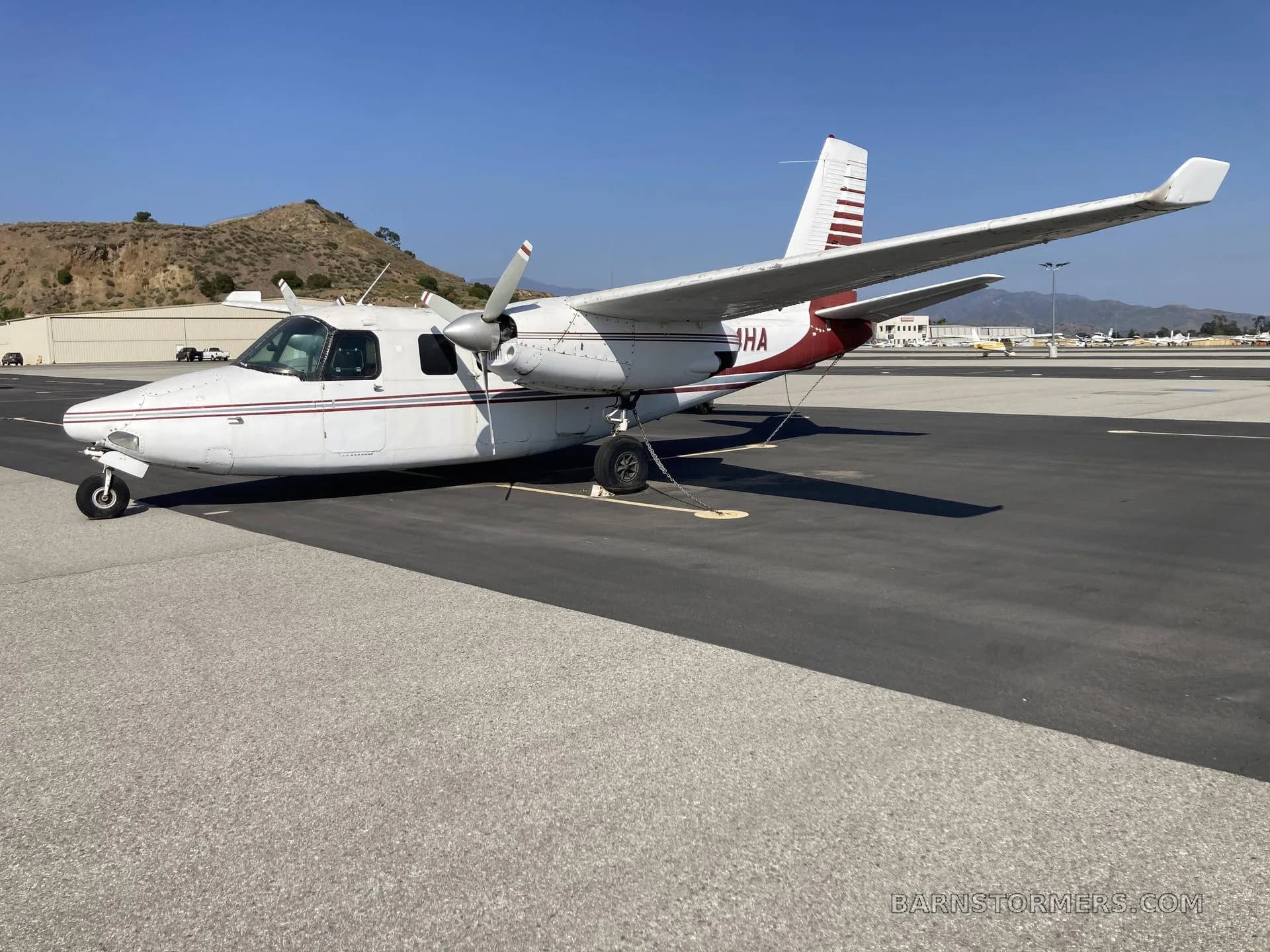A white and red twin-engine Commander aircraft (N224HA) parked on an asphalt tarmac, viewed from the front-right.