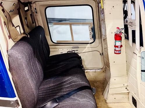 The interior of a Bell 407 helicopter, showing the seats and a fire extinguisher.