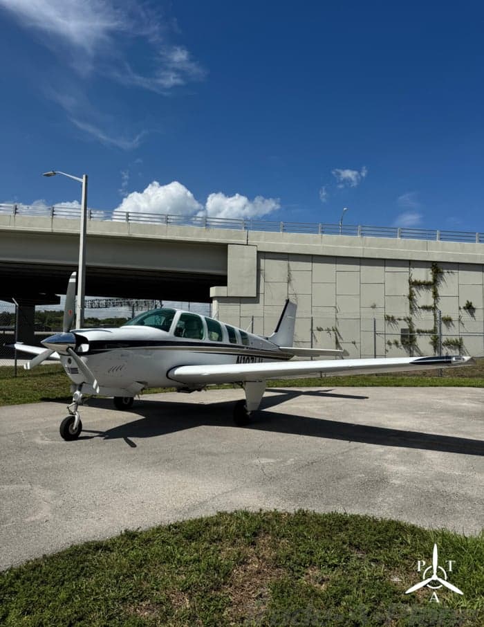 A front-side view of the white single-engine aircraft N107LU with a black stripe, parked on a tarmac near a highway overpass.