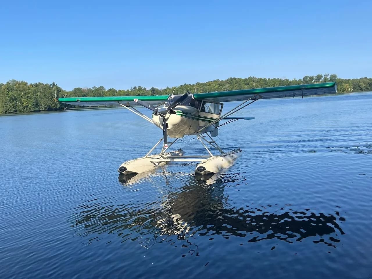 A Maule seaplane with a green and white paint scheme on floats is floating on a calm lake.