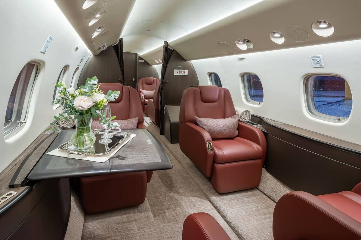 View of the aircraft interior with red leather seats, a table, and a neutral color scheme.