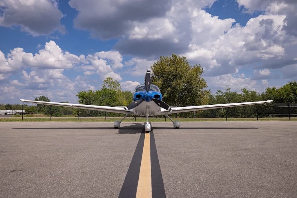 A head-on view of the blue and white Cirrus SR22 aircraft, N970S, parked on an asphalt ramp with a yellow centerline.