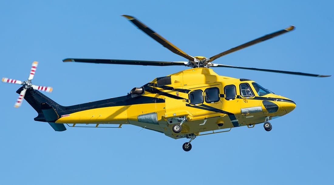 A bright yellow helicopter with black stripes and a striped tail rotor flies against a clear blue sky.