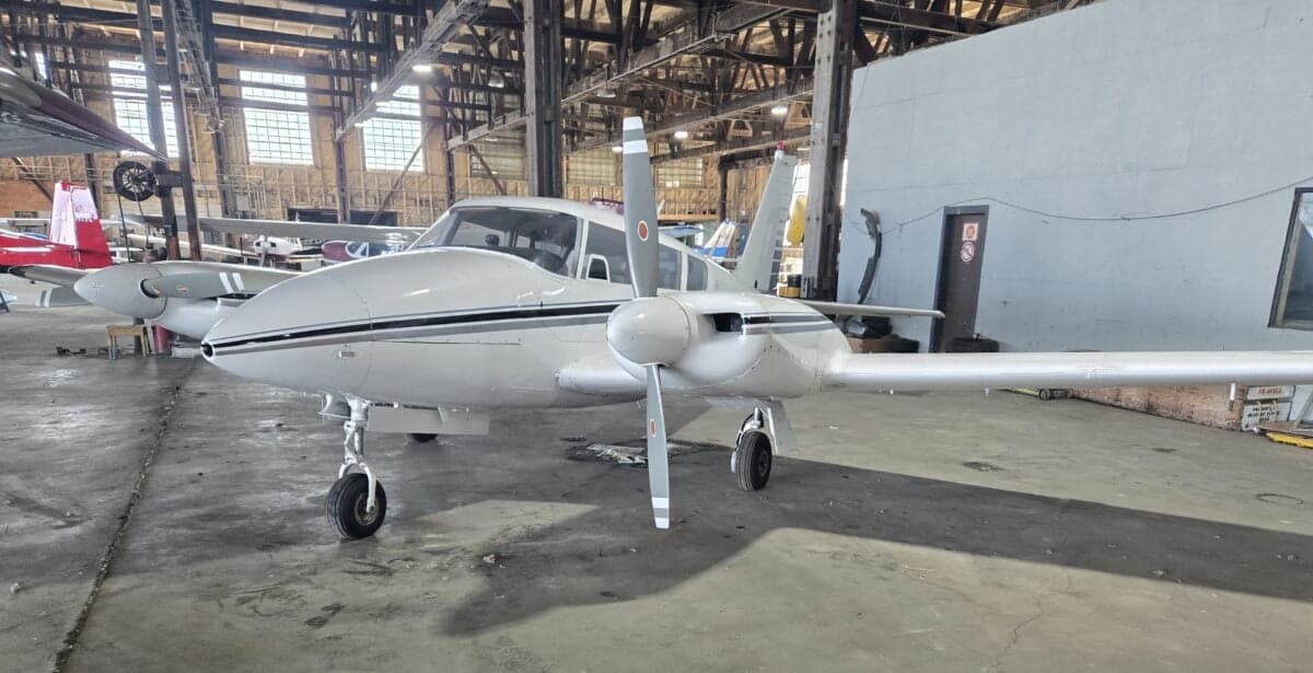 A white and black Piper PA-39 Twin Comanche is parked in a hangar.