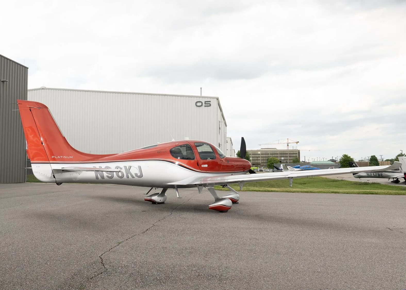 A red and silver Cirrus SR22T aircraft, registration N96KJ, parked on an asphalt apron with a white hangar in the background.