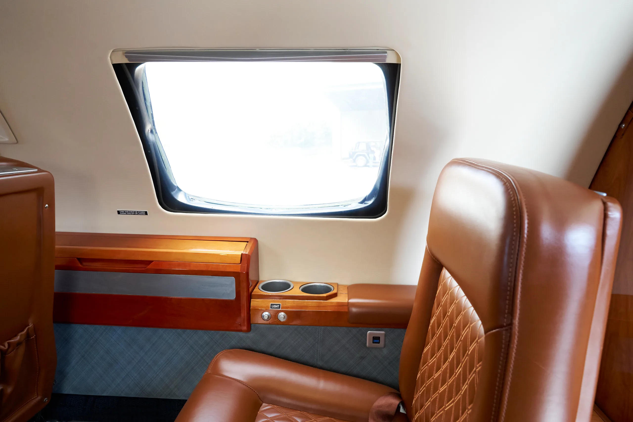 A close-up of a cabin window and a brown quilted leather seat with wood paneling and cupholders.