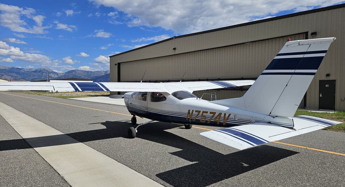 A Cessna 182 Skylane, tail number N7574V, parked on the tarmac in front of a hangar.
