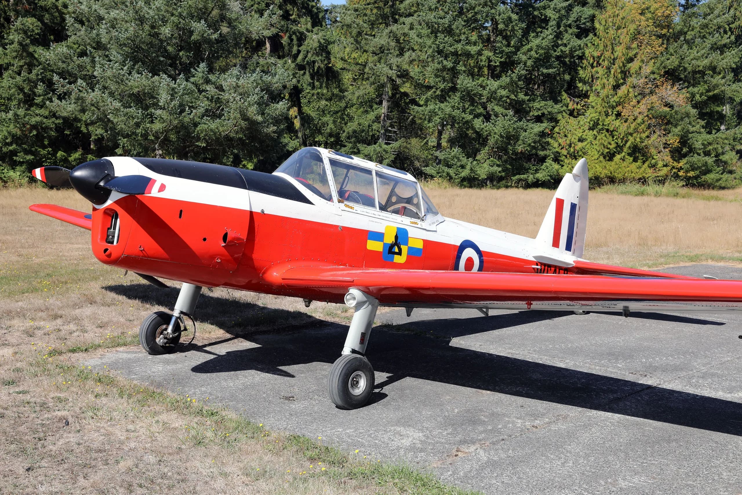 A red, white, and black de Havilland Canada DHC-1 Chipmunk aircraft with British roundels and "WC459" markings, parked on an airfield.