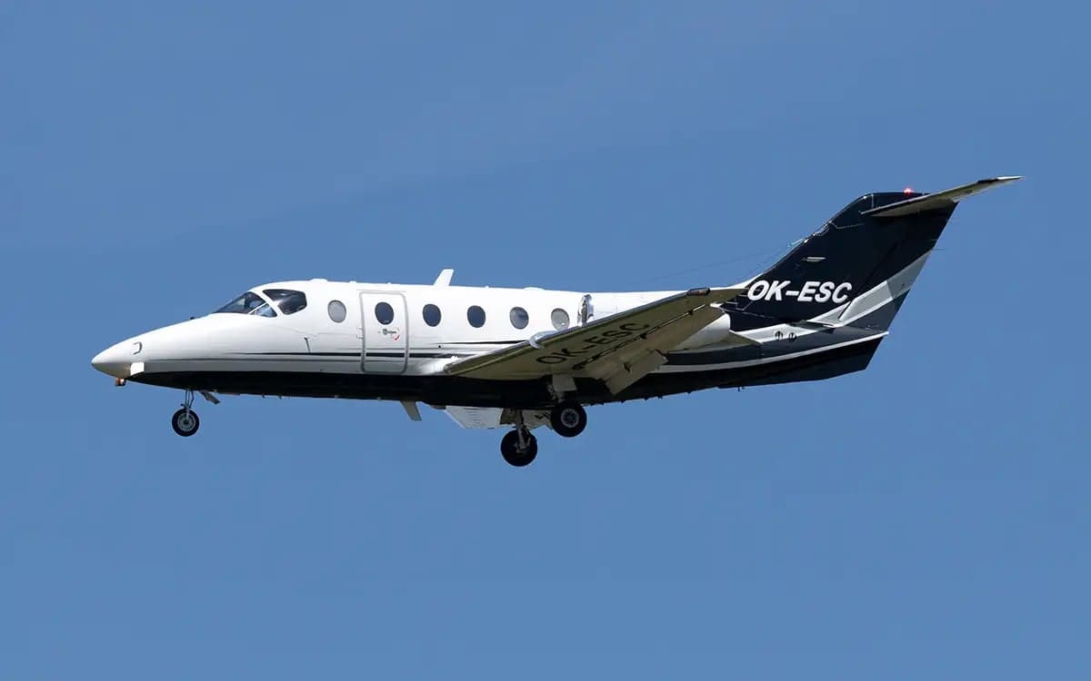 The Nextant 400XT aircraft with registration OK-ESC is shown in flight against a clear blue sky.