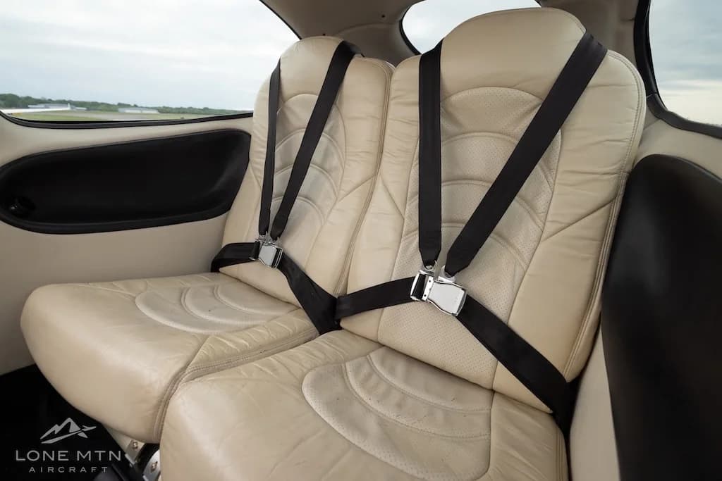 Angled view of the two rear beige leather seats with black harnesses in the aircraft cabin.