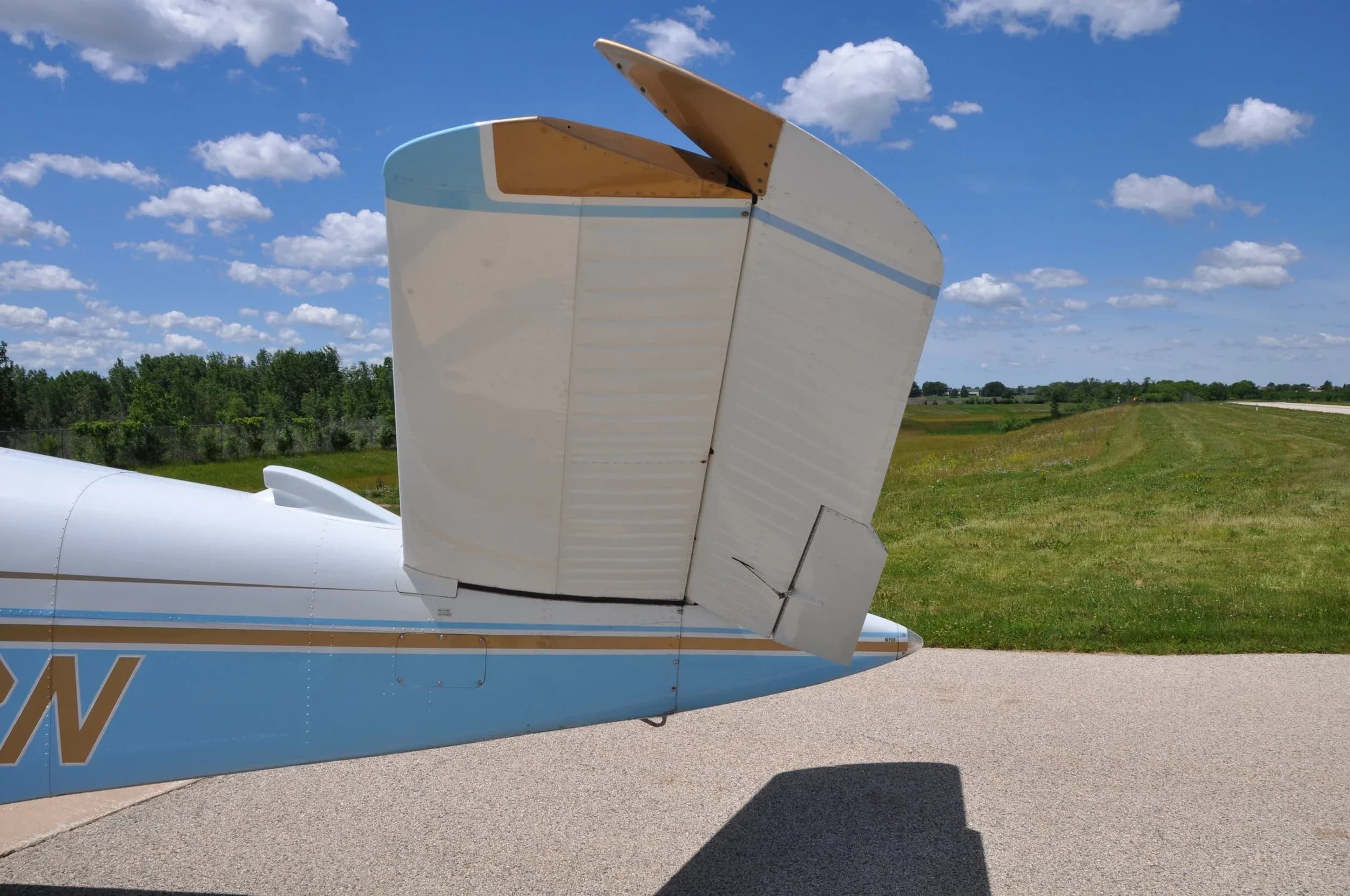 A close-up side view of the V-tail of a light blue and white single-engine aircraft against a blue sky.
