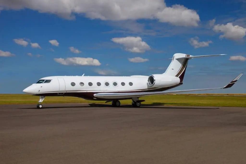 A Gulfstream G650 on the tarmac with a white and maroon paint scheme.