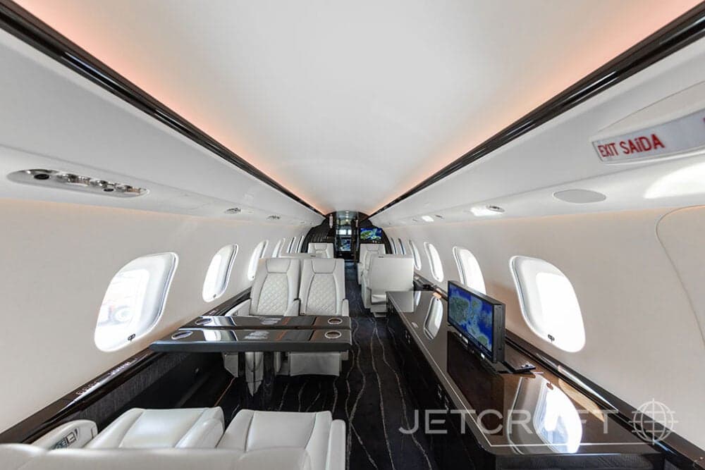Aft view of the cabin of a Bombardier Global Express with white leather seats, tables, and a monitor.