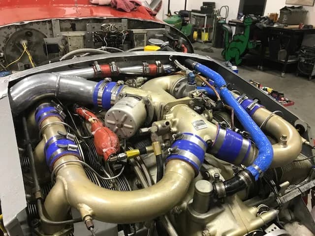 A detailed view of an aircraft engine with various pipes, hoses, and components exposed in a hangar.