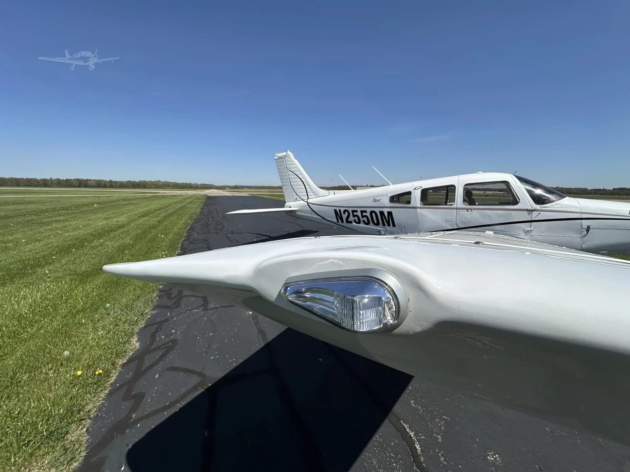 A close-up view of the white wingtip and navigation light of a Piper Cherokee, with the aircraft N2550M visible in the background.