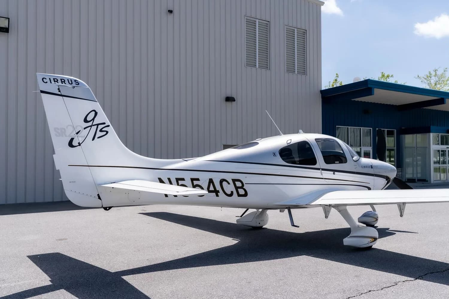 A close-up side view of the rear fuselage and tail of a silver and white Cirrus SR22T aircraft with registration N554CB.