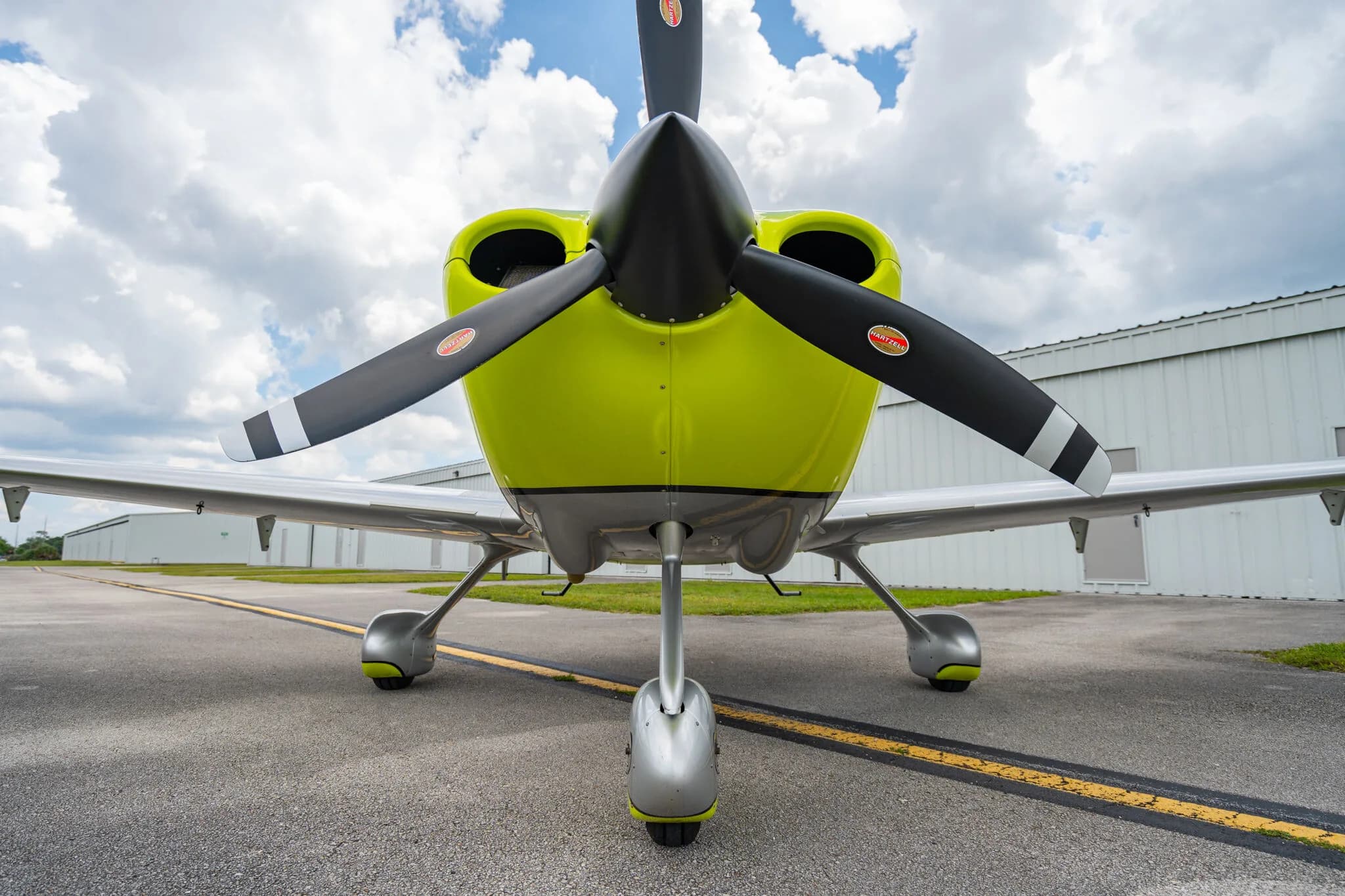 Front view of a lime green and silver Cirrus SR20 aircraft with a three-bladed propeller, parked on an asphalt ramp.