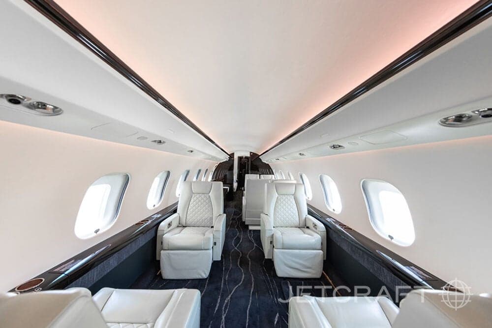 Forward view of the cabin of a Bombardier Global Express with white leather seats and dark wood accents.