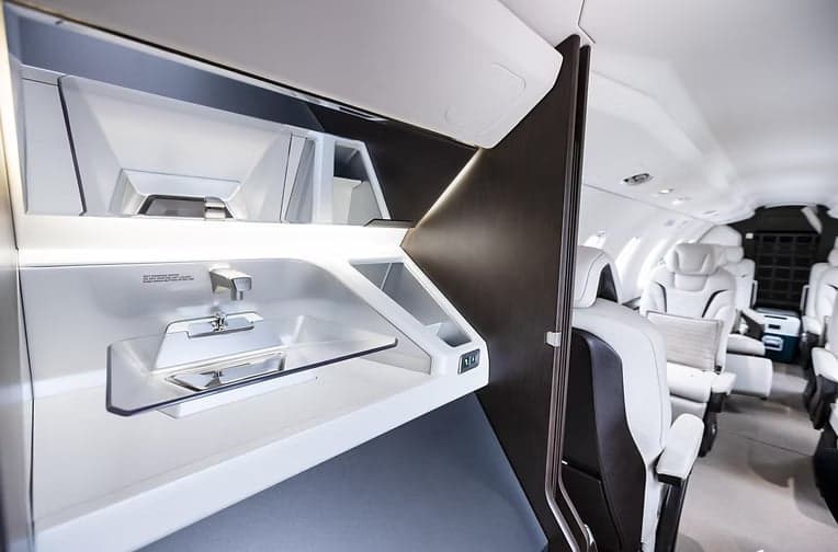 A view of the interior of a Pilatus PC-24 with white leather seats and tables.