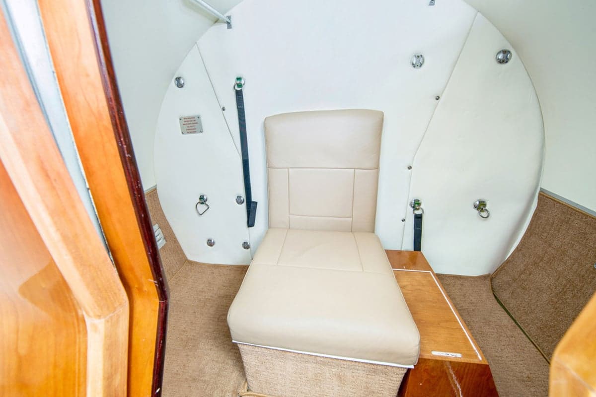 A single beige leather seat in the aft section of an aircraft cabin with white walls and wood trim.