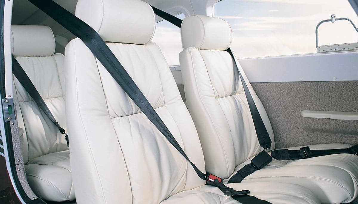 Aircraft interior featuring white leather seats with black seatbelts.