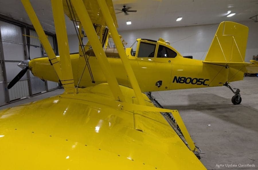 A yellow biplane crop duster is parked inside a hangar.