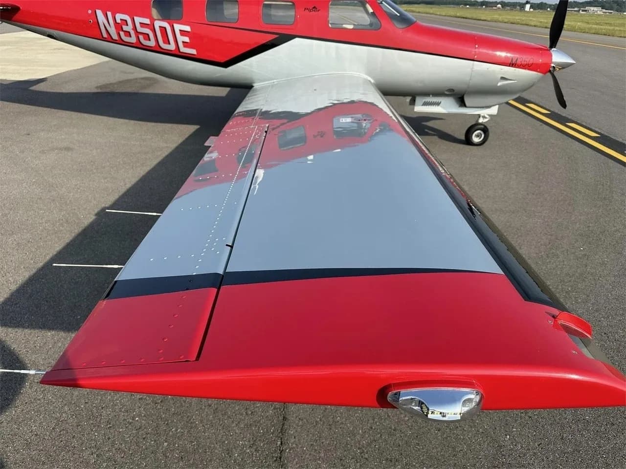 A close-up view of the red and silver wing of the Piper M350 aircraft, with N350E visible on the fuselage.