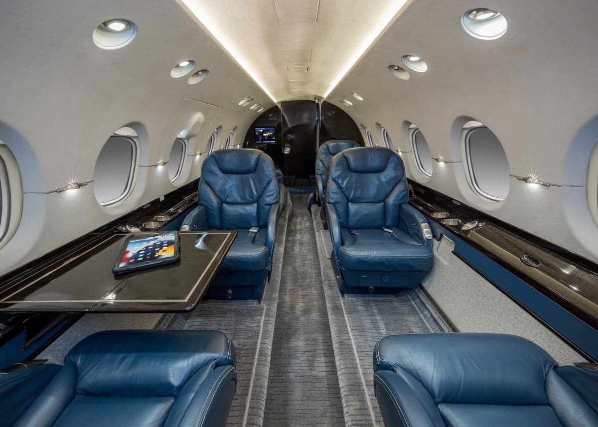 View of the aircraft interior featuring blue leather seats and a table with a tablet on it.