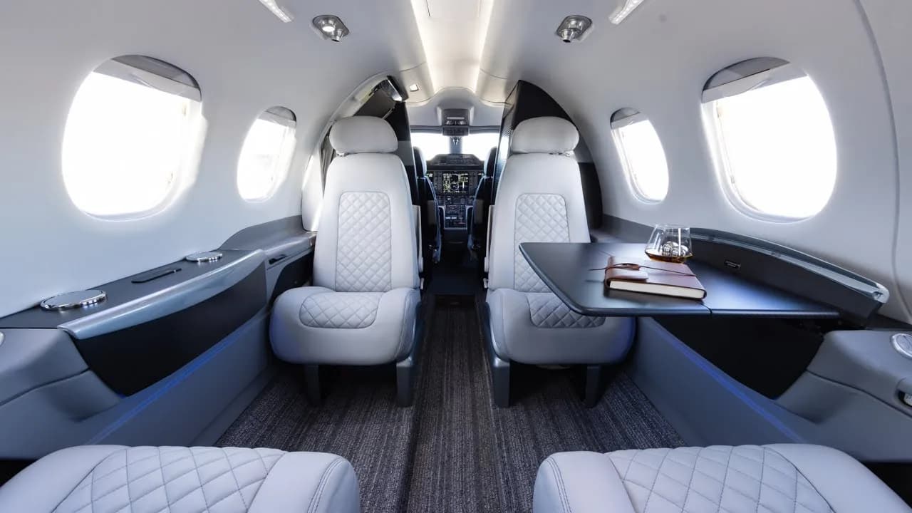 Interior view of an aircraft cabin with white leather seats and a table.