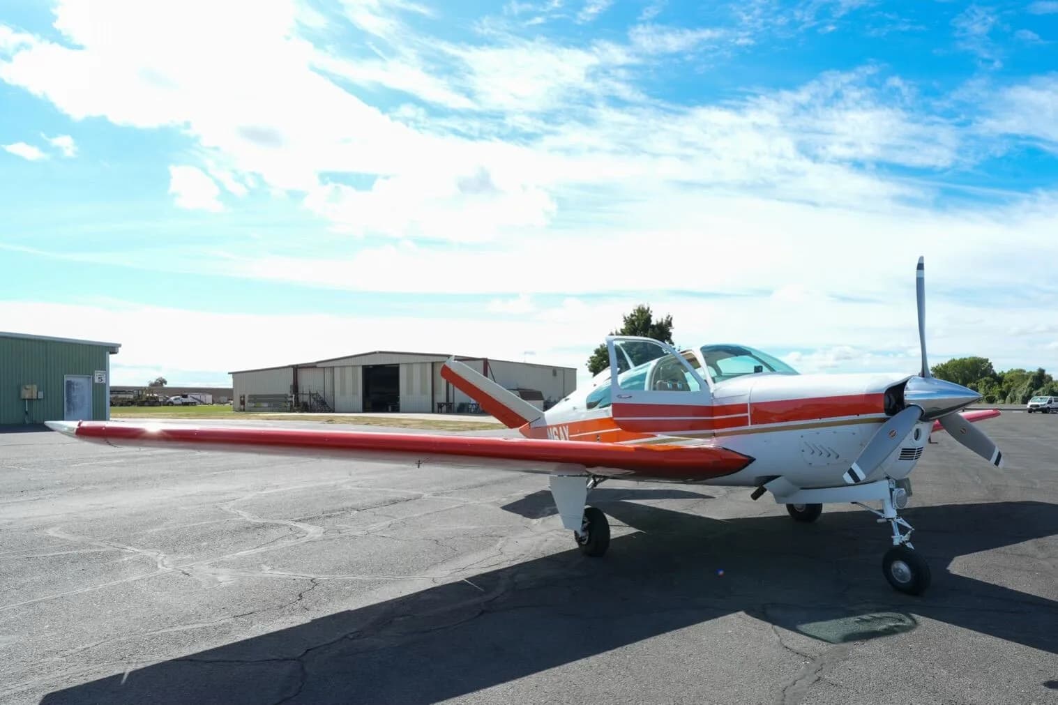 A low front view of the white and orange Beechcraft Bonanza N6AY with its door open on the tarmac.