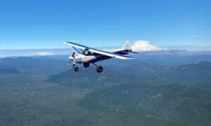 A Cubcrafters aircraft in flight over a mountainous landscape.