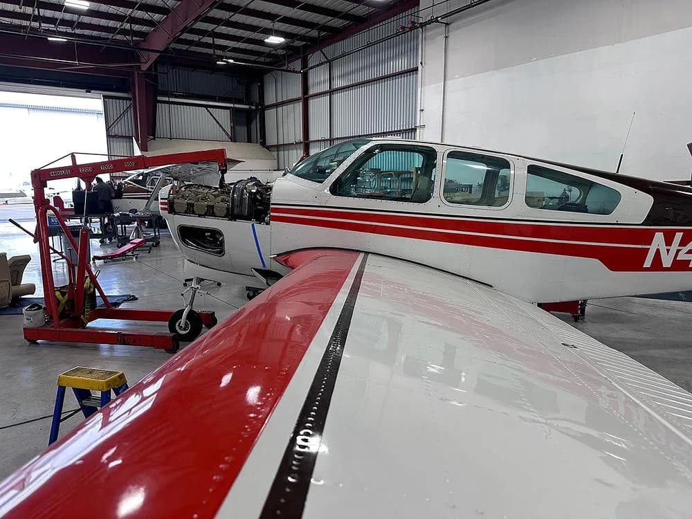 A white and red aircraft with its engine cowling open, undergoing maintenance in a hangar.