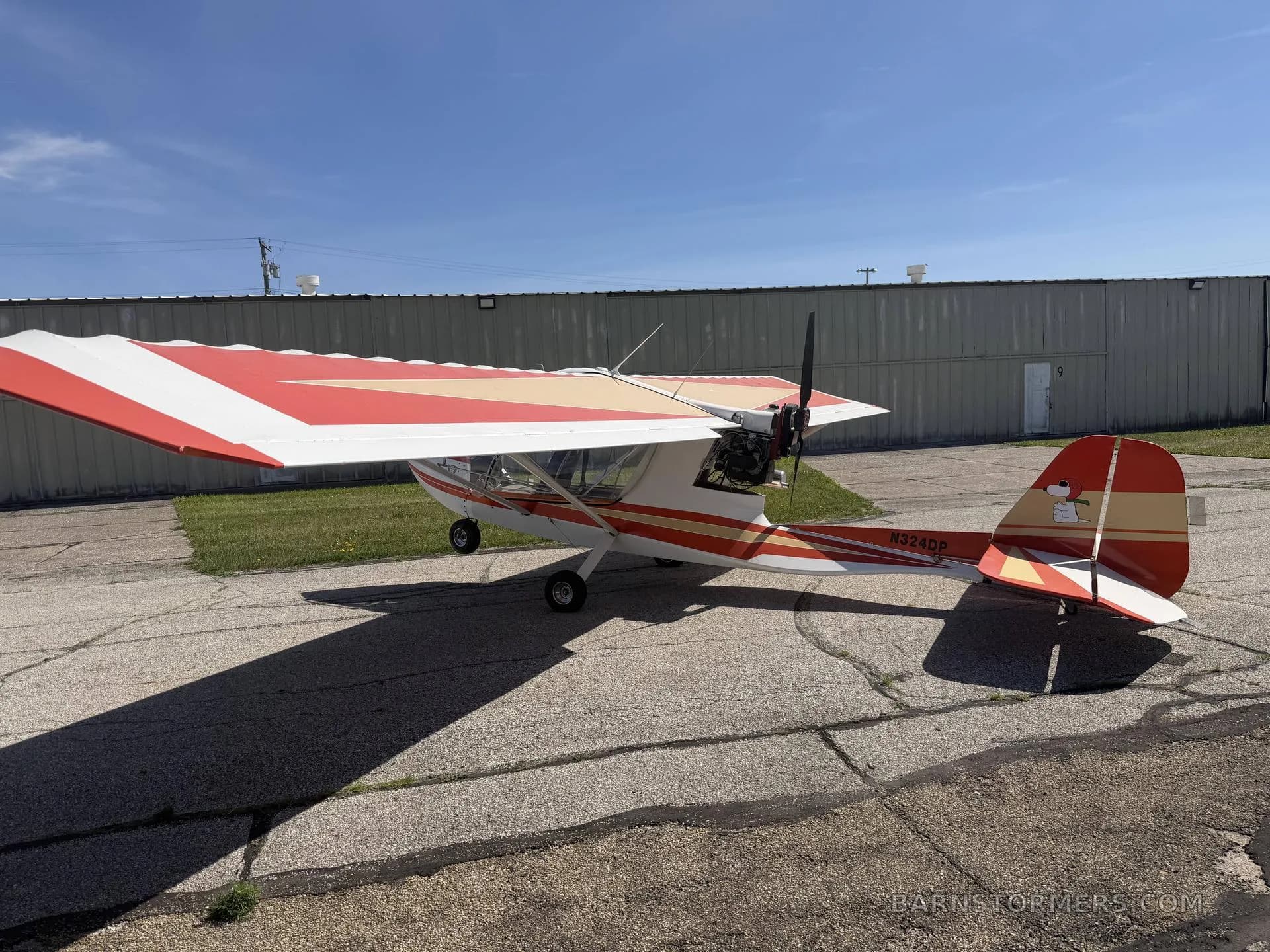 A rear-quarter view of a white and orange Challenger ultralight aircraft with tail number N324DP, parked on an airfield.