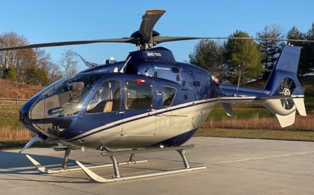A blue and silver EC135 helicopter on the tarmac at dusk.