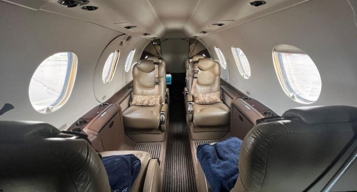 The interior cabin of a private jet, featuring tan leather seats arranged in a club configuration with a narrow aisle.