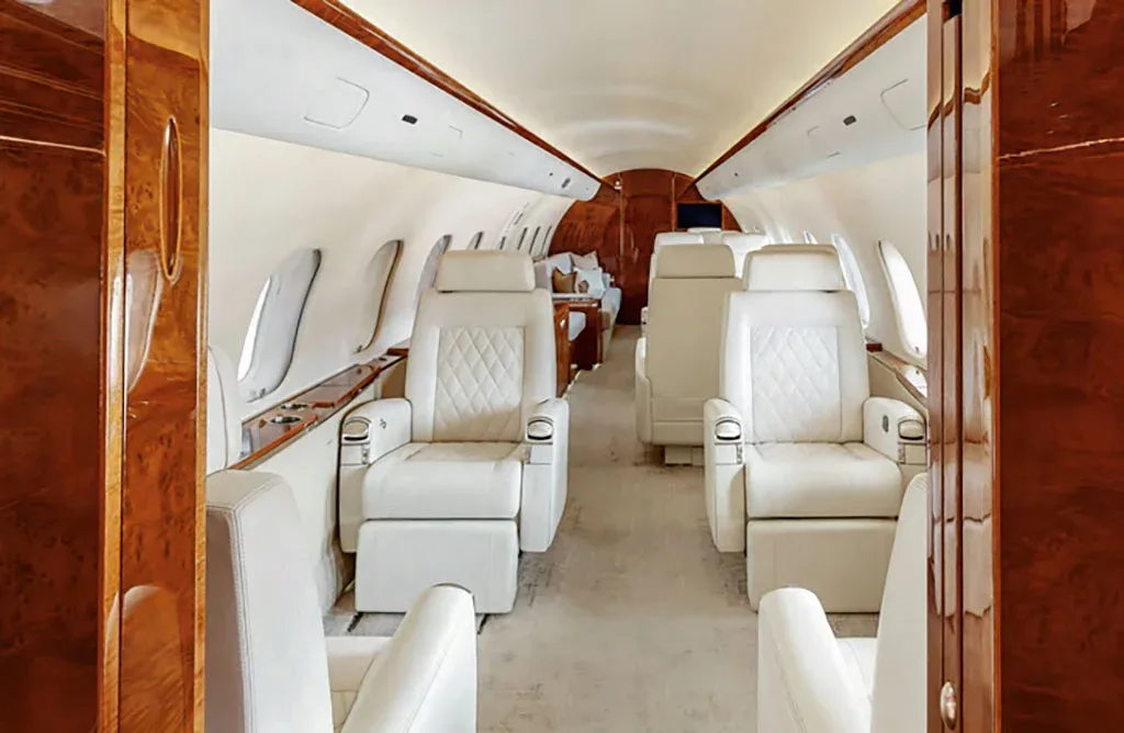 The long private jet cabin features multiple rows of white quilted leather seats and polished wood trim.