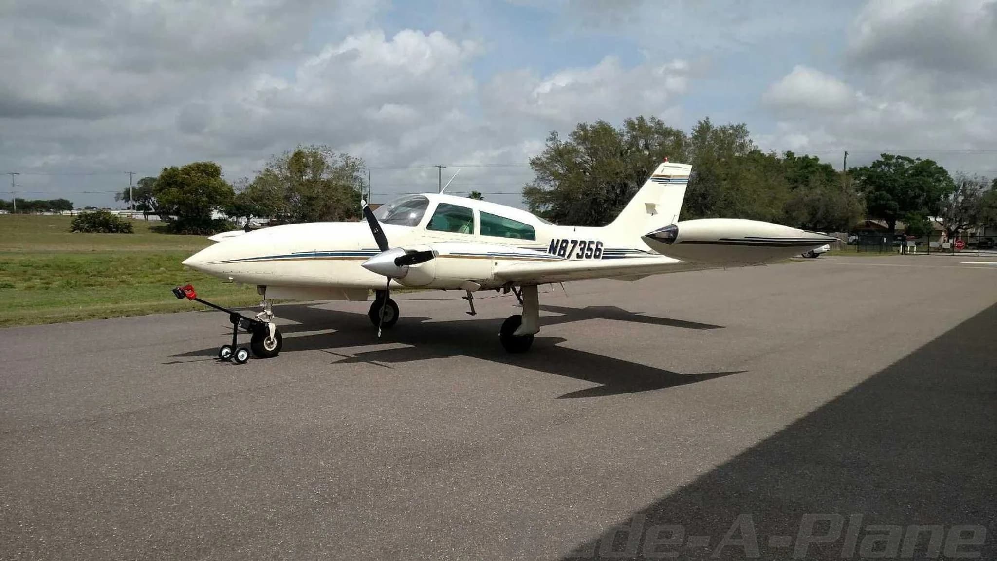 A white twin-engine aircraft with blue and gold stripes, registration N87356, parked on an asphalt ramp.