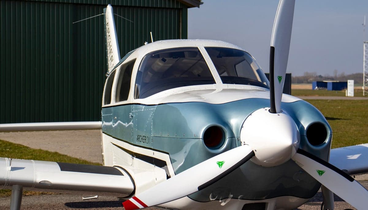 Close-up of the front of a Piper Archer II aircraft, showing the propeller and nose.
