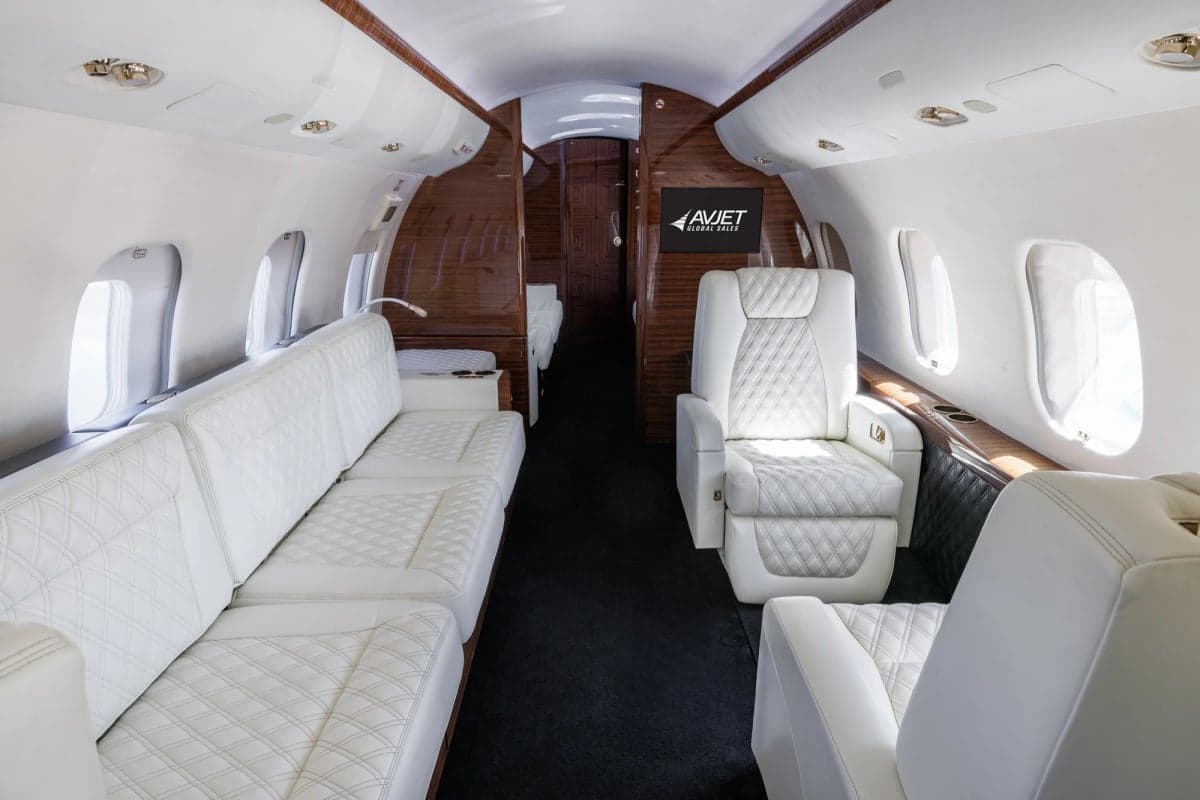 Interior view of a private jet cabin with white leather seats and a bed.