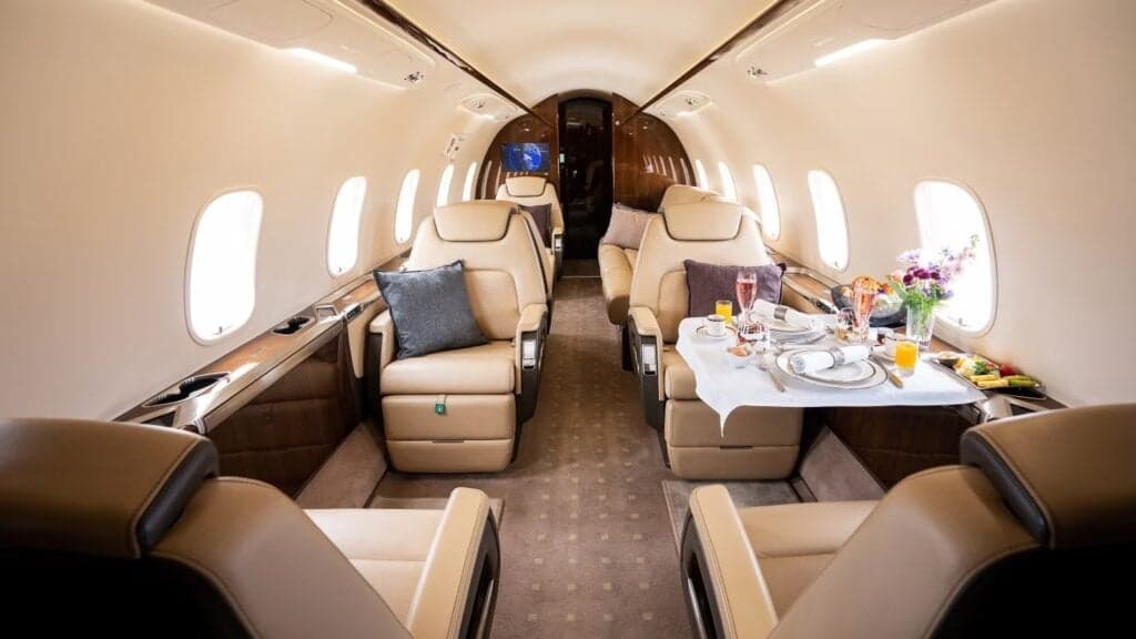 The interior of a private jet cabin with leather seats and a table set for a meal.